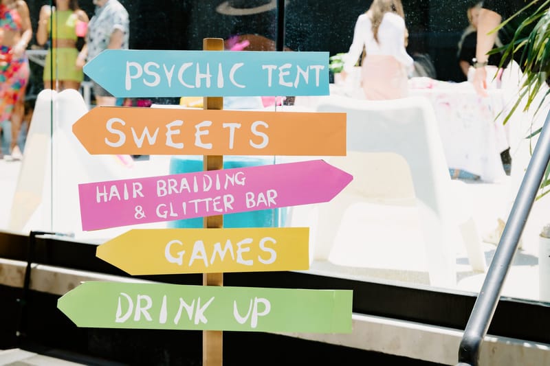 Painted signpost pointing to Psychic Tent, Sweets, Hair Braiding & Glitter Bar, Games and Drink Up